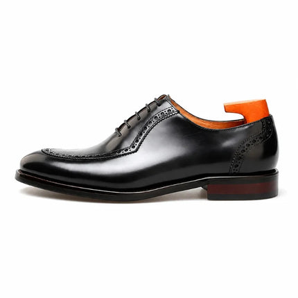 A black leather wingtip oxford shoe with decorative brogue perforations, shown in a side profile on a white background. An orange shoe tree is inserted inside the heel area.